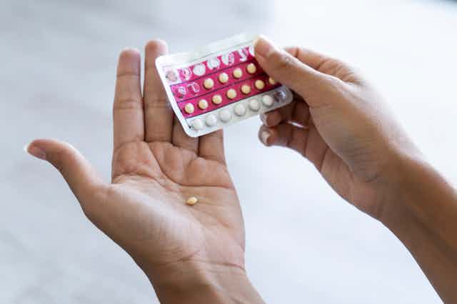 Close up of person holding blister pack of birth control pills, with one pill in the palm of one hand