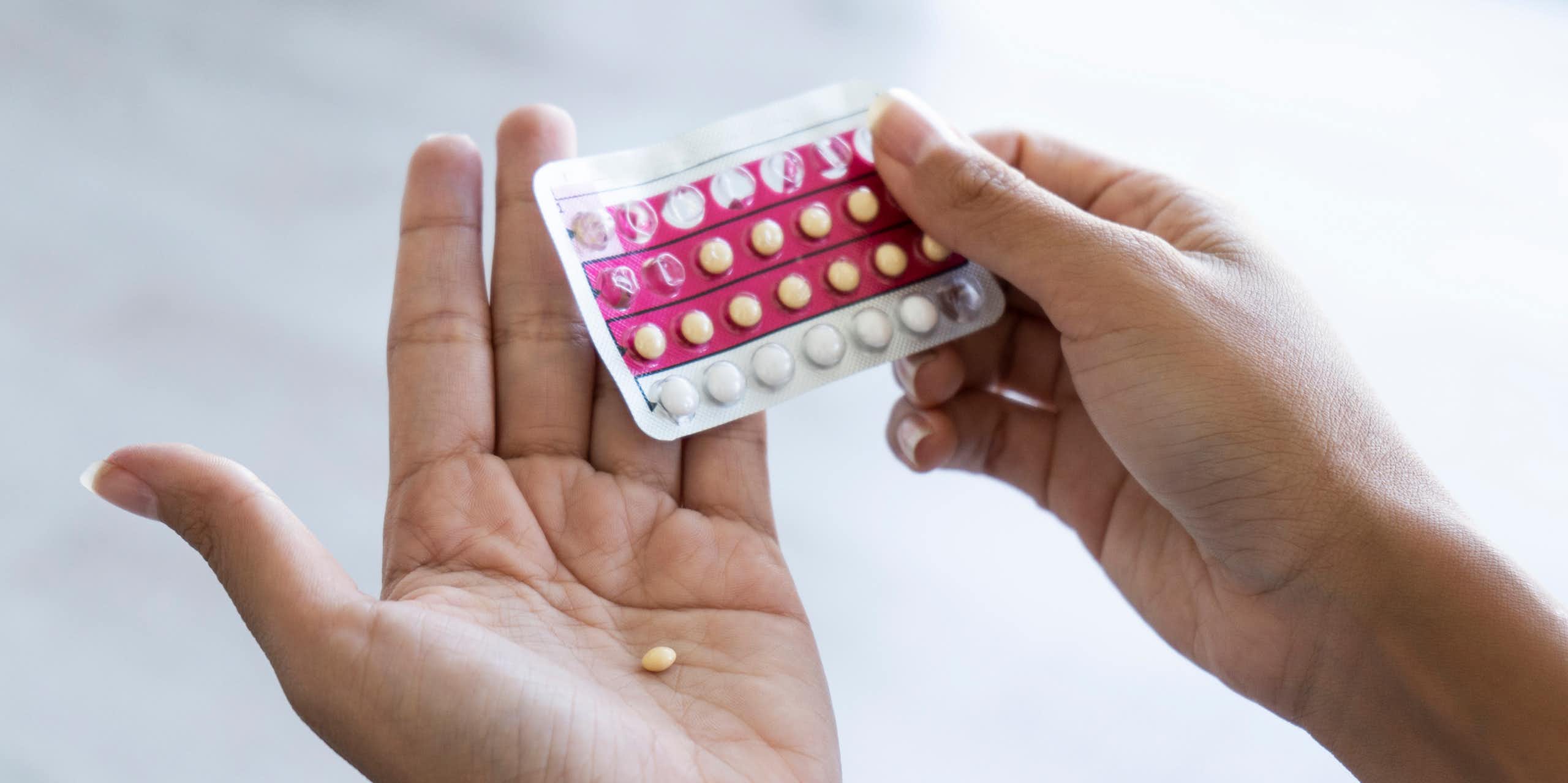 Close up of person holding blister pack of birth control pills, with one pill in the palm of one hand