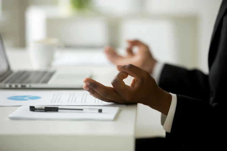 A pair of hands resting on the edge of a desk with the thumb and index finger touching to make a circle