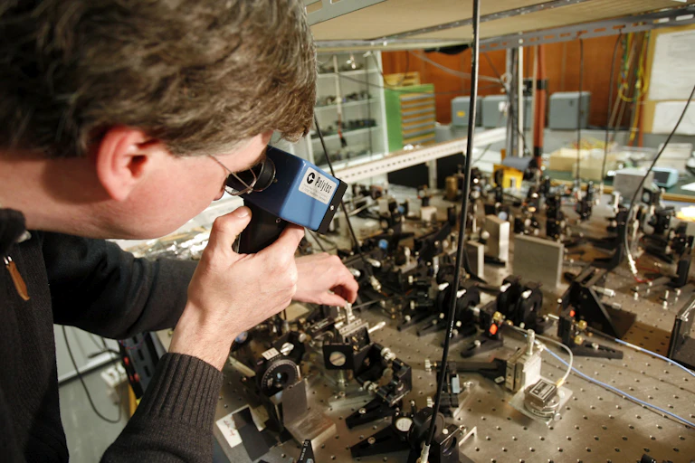 A man looks through a handheld machine at a table top full of lasers