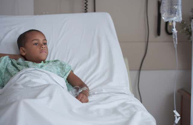A boy lies in a hospital bed with an IV in his arm. 
