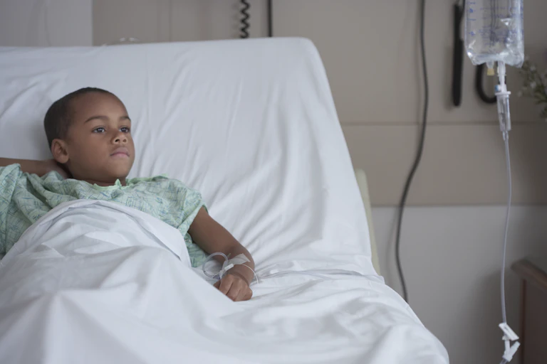 A boy lies in a hospital bed with an IV in his arm.