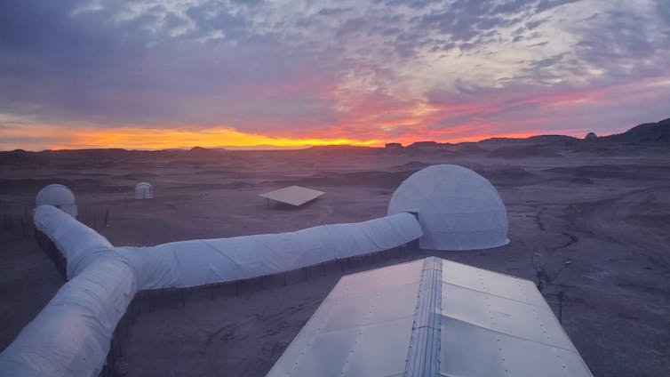 Two dome tents in the desert connected by long tubes.