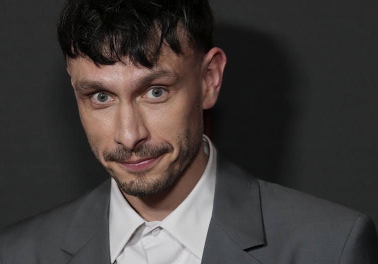 A man in a grey suit and white shirt poses for a photo