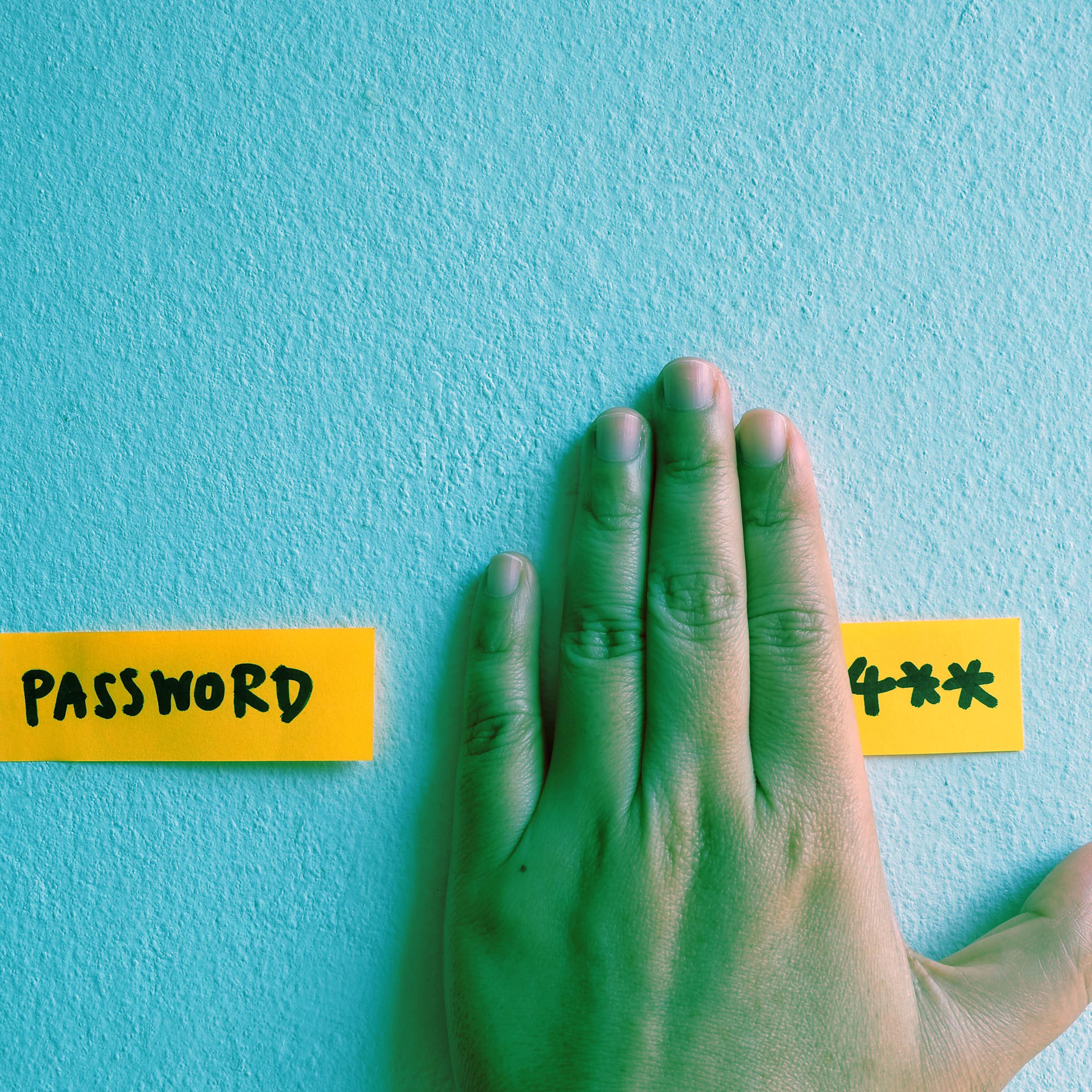 A hand partially covering a sticky note with a password on it.
