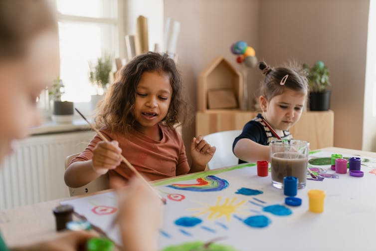 Two young girls sit at a table and paint
