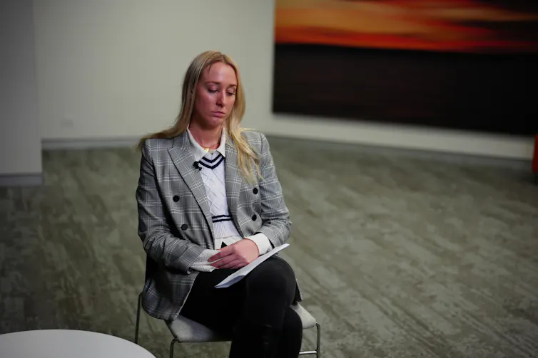 A young blond woman sits wearing a grey blazer