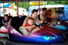 Mother and a young child drive dodgem car together in theme-park