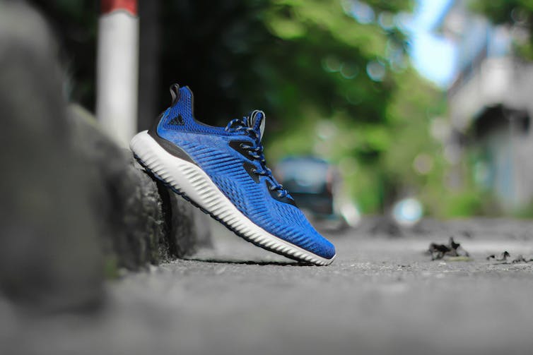 A blue and white running shoe propped against a kerb outdoors.