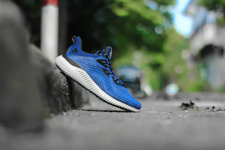 A blue and white running shoe propped against a kerb outdoors.