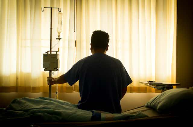 The back of a patient sitting on a hospital bed.