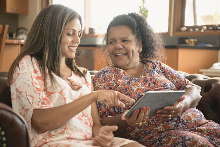 Two women are smiling and using a tablet computer.