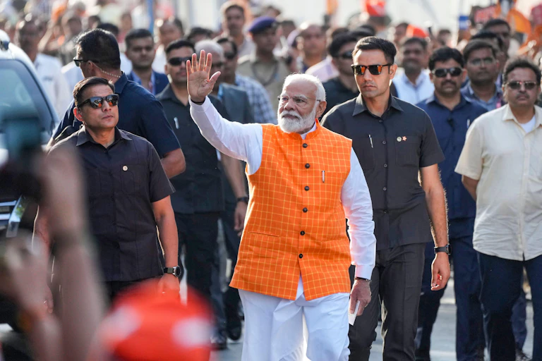 INdian prime minister Narendra Modi, surrounded by aides and wearing an orange waistcoat, waves to supporters.