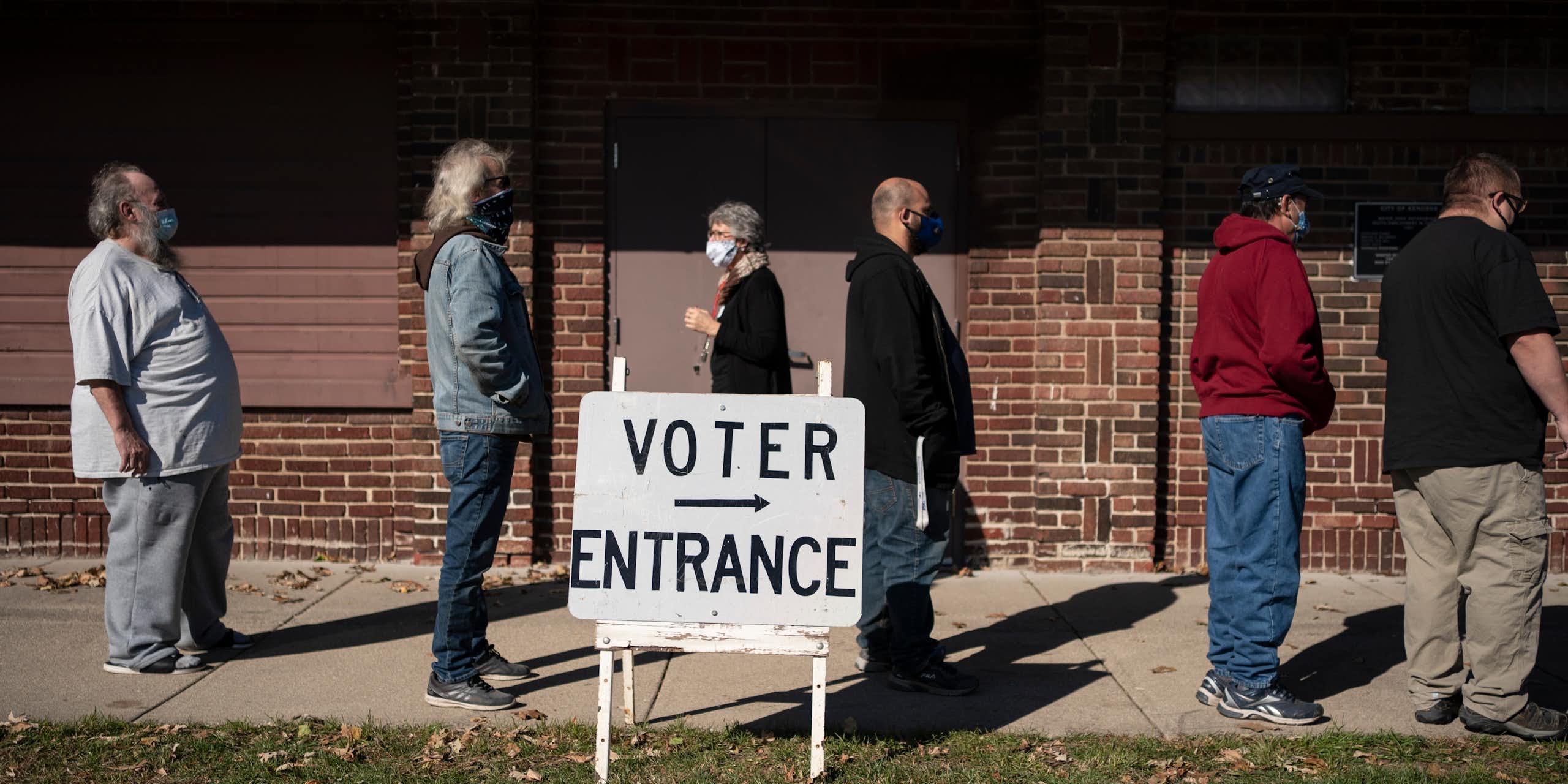 People stand in a line next to a sign reading 'voter entrance.'