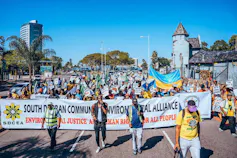 A big community march of hundreds of people carrying a banner that says South Durban Community Environmental Alliance