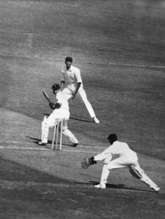 Black and white photo of three cricketers wearing white uniforms.