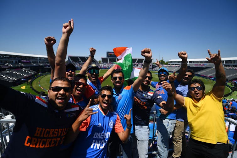 Young men wearing sunglasses whoop it up at a cricket stadium.