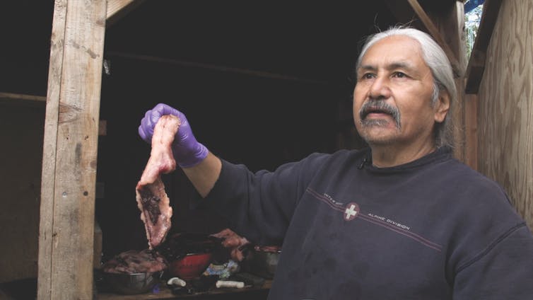 man holds a piece of raw meat at shoulder height