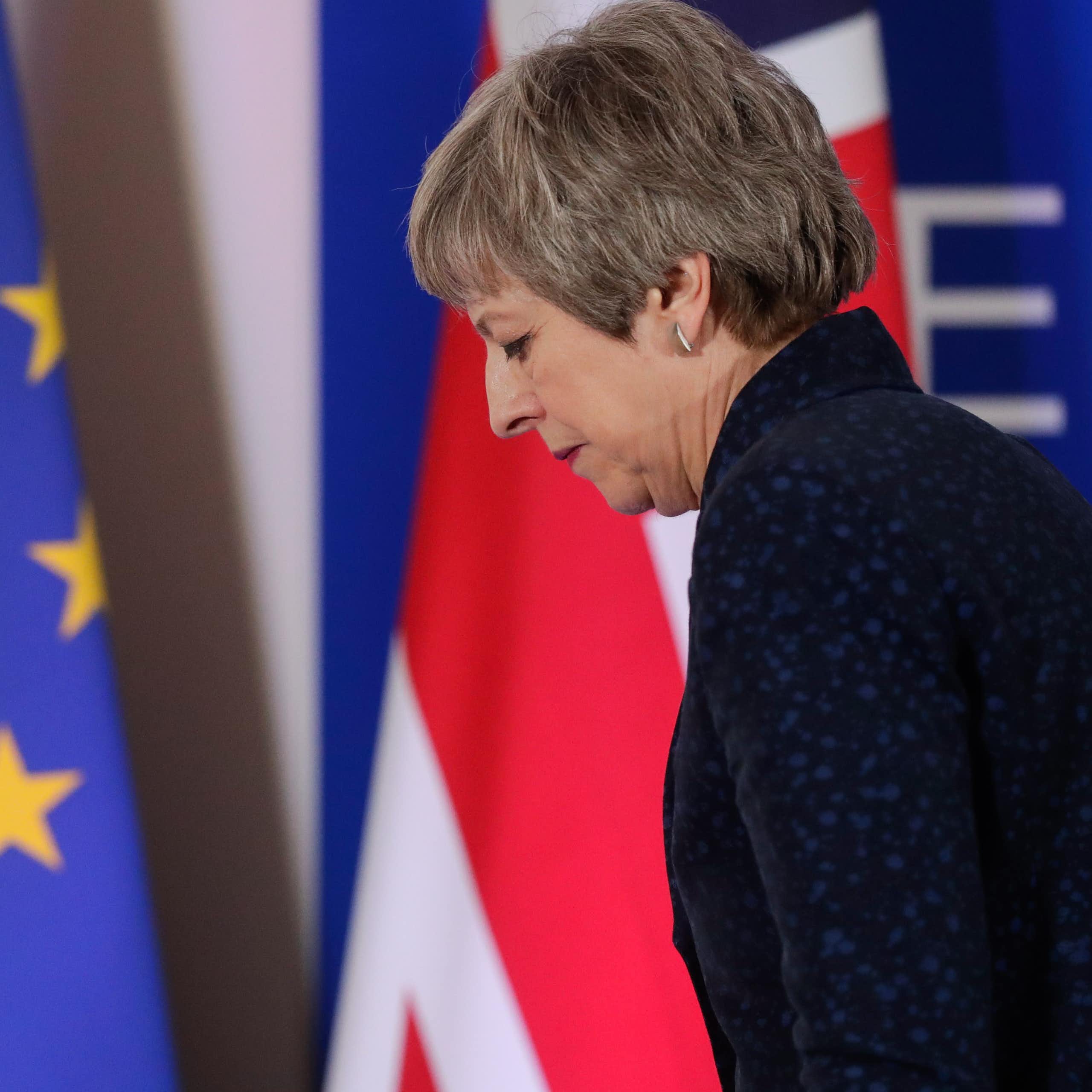 Theresa May sadly walking in front of an EU and UK flag
