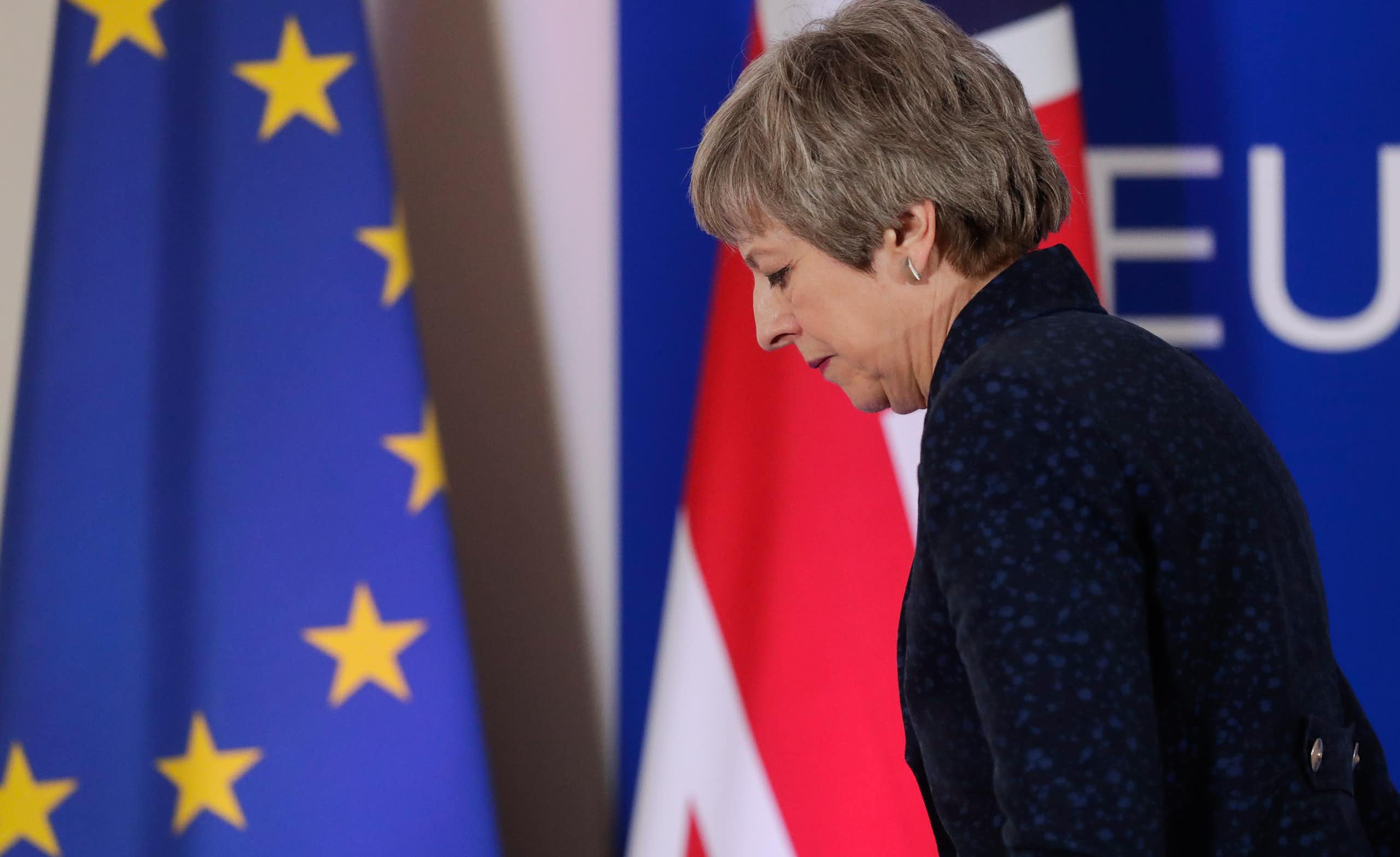Theresa May sadly walking in front of an EU and UK flag