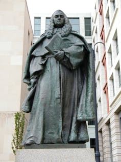 A statue of a man in robes and a long wig holding a large book.