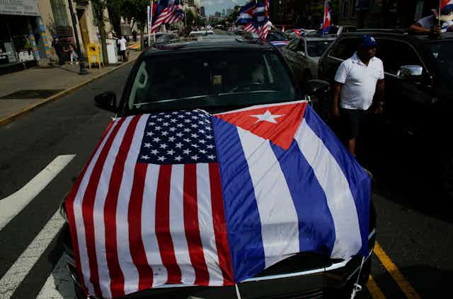 A car has the American and Cuban flags on the bonnet.