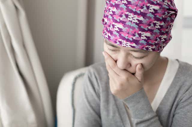 Woman with cancer wearing scarf/hat, hand over mouth