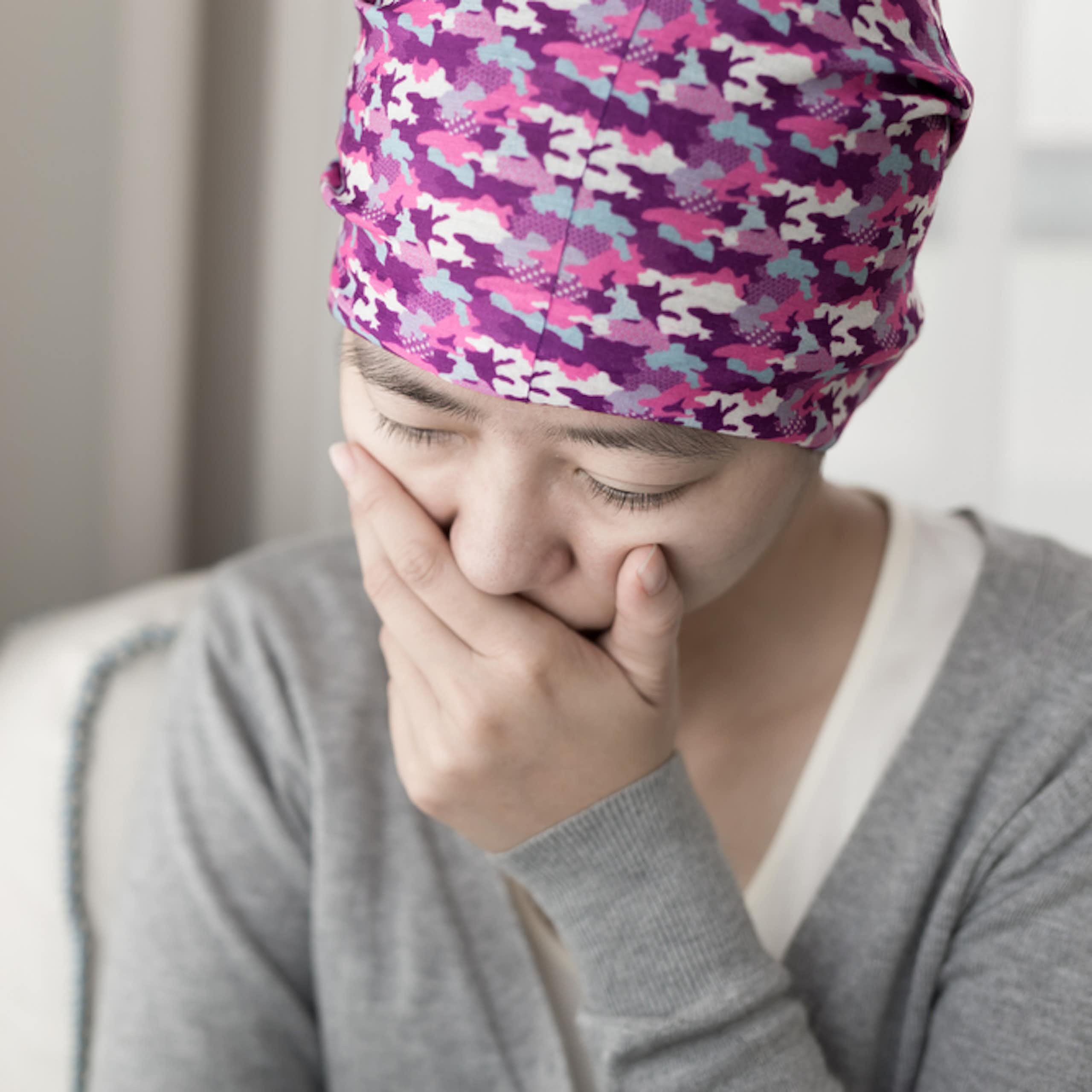 Woman with cancer wearing scarf/hat, hand over mouth