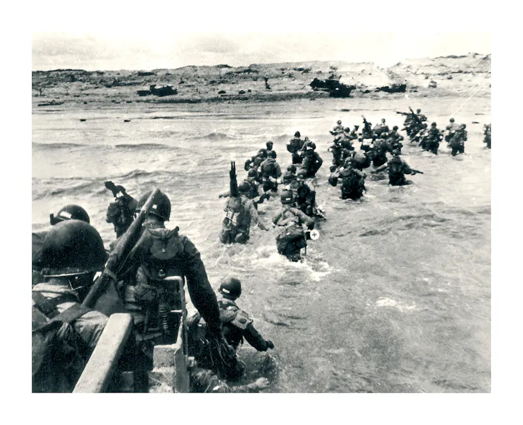 A black and white photo depicting soldiers leaving landing craft during D-day in 1944.