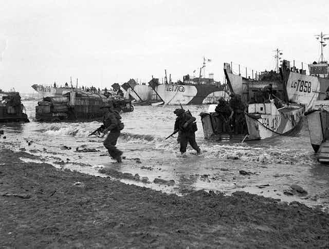 A black and white photo showing soliders coming ashore on a beach during the D-Day landings of 1944.