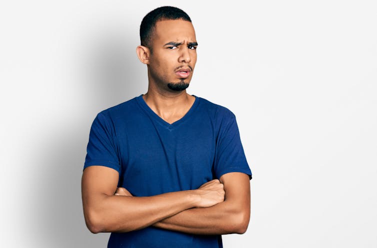 Homem com braços cruzados gesto em cara de choque, parecendo cético e sarcástico.