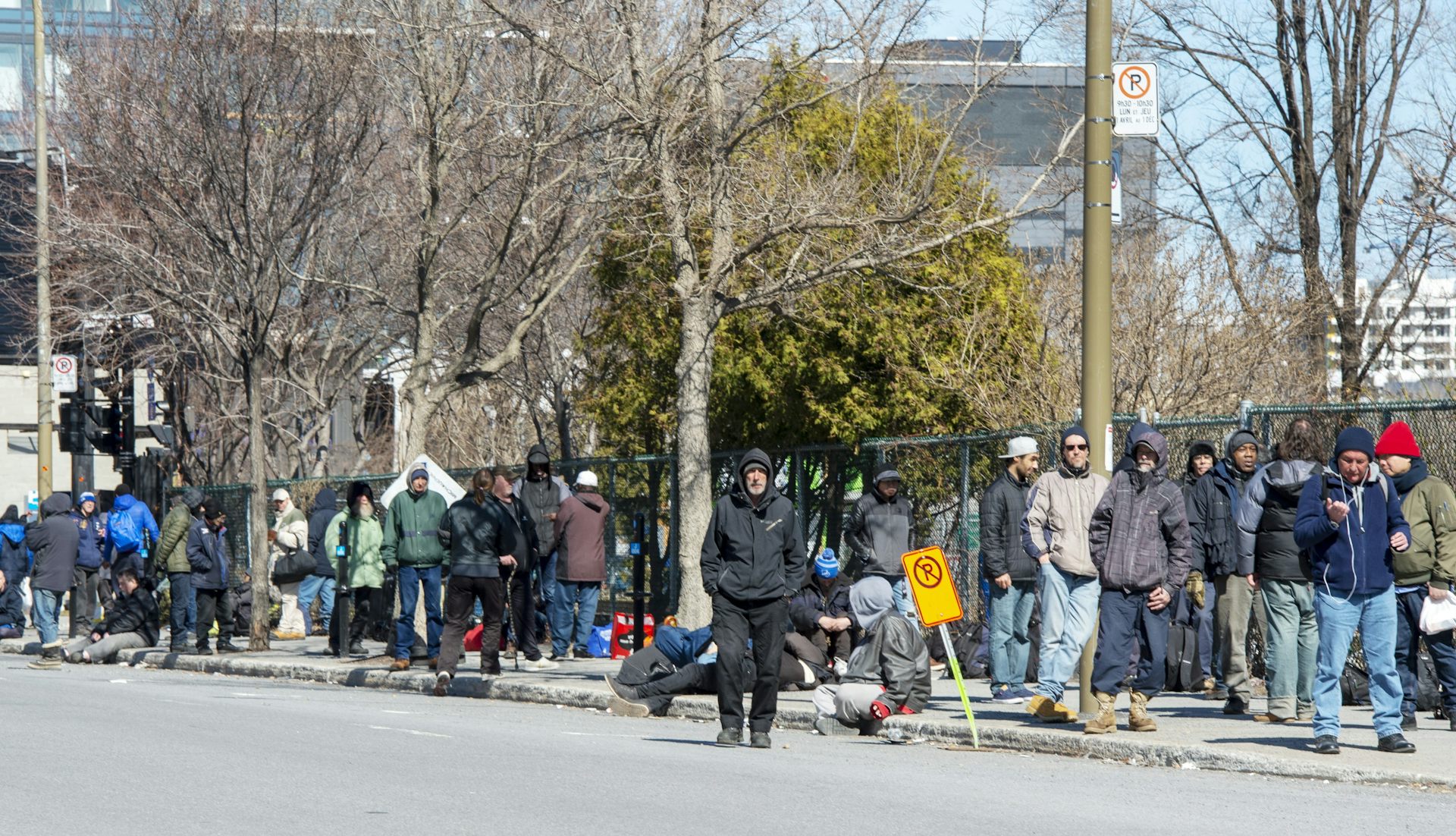 Une file d'hommes debout sur un trottoir, contre une clôture