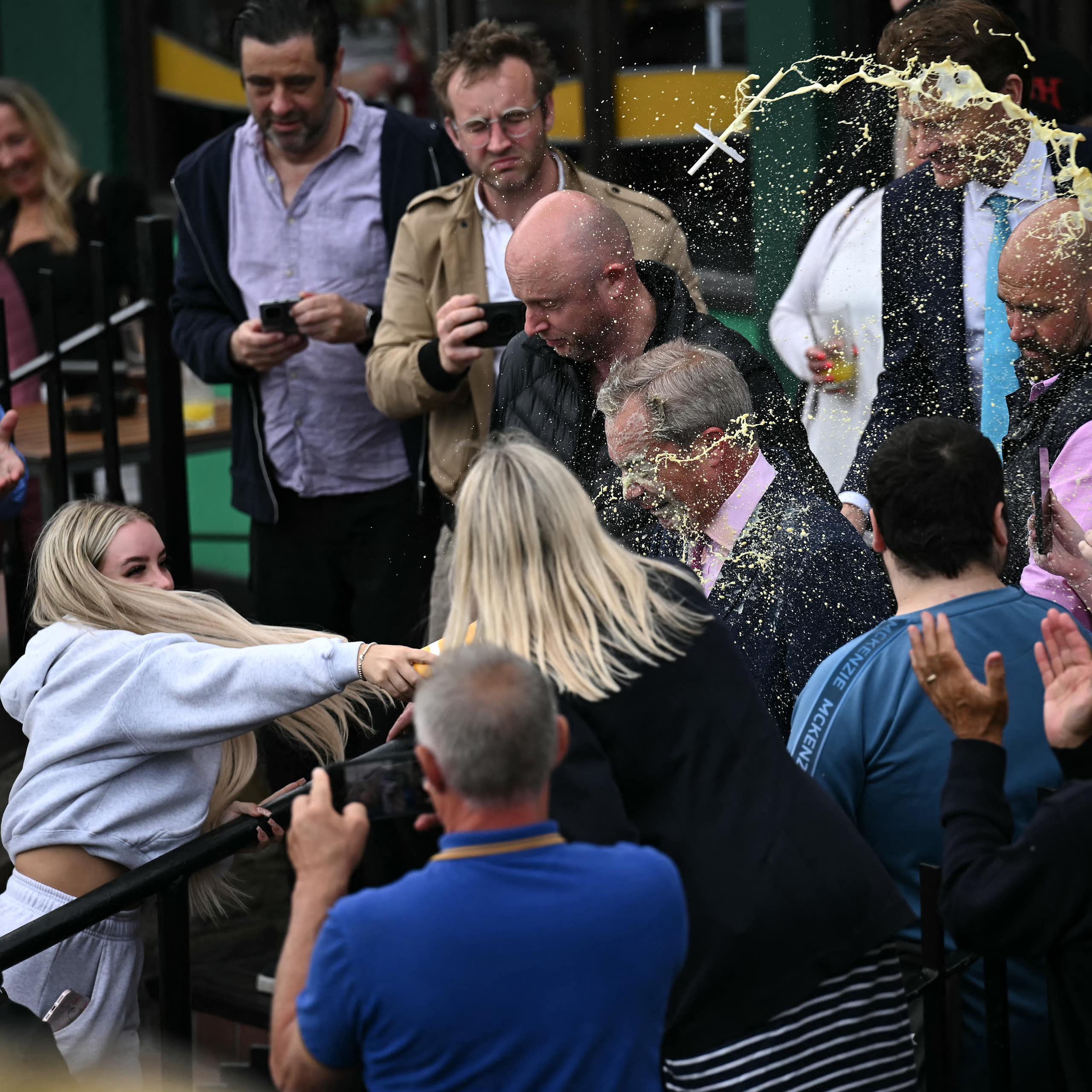 Woman in crowd throws a milkshake at a man.