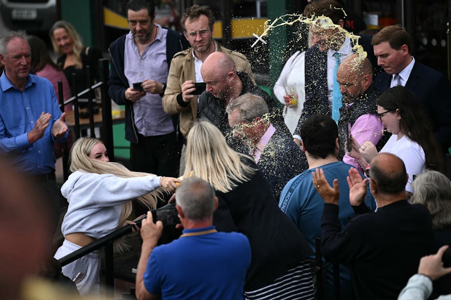 Woman in crowd throws a milkshake at a man.