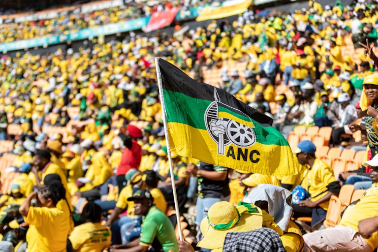 People in a stadium, many wearing yellow shirts, and a black, green and yellow flag bearing the letters ANC in the foreground