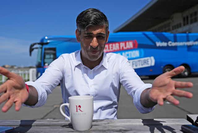 RIshi Sunak raising his hands to the camera in front of his campaign bus