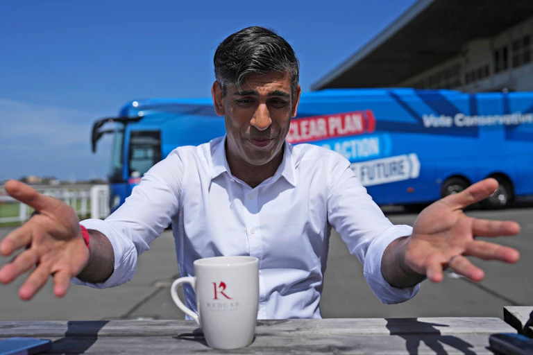 RIshi Sunak raising his hands to the camera in front of his campaign bus