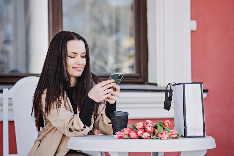 a woman smiles at her phone while sitting at a table with a bunch of pink tulips