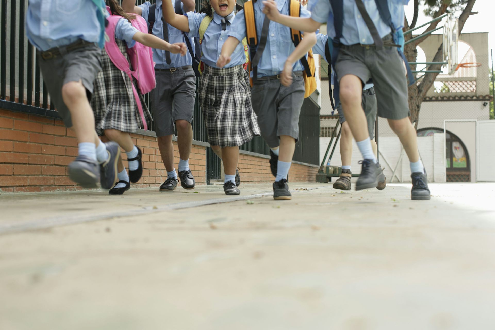 Children in uniforms run on concrete in a school playground.
