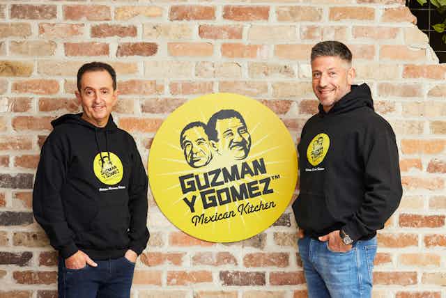 Guzman y Gomez co-CEO Hilton Brett and founder and co-CEO Steven Marks stand in front of the company logo