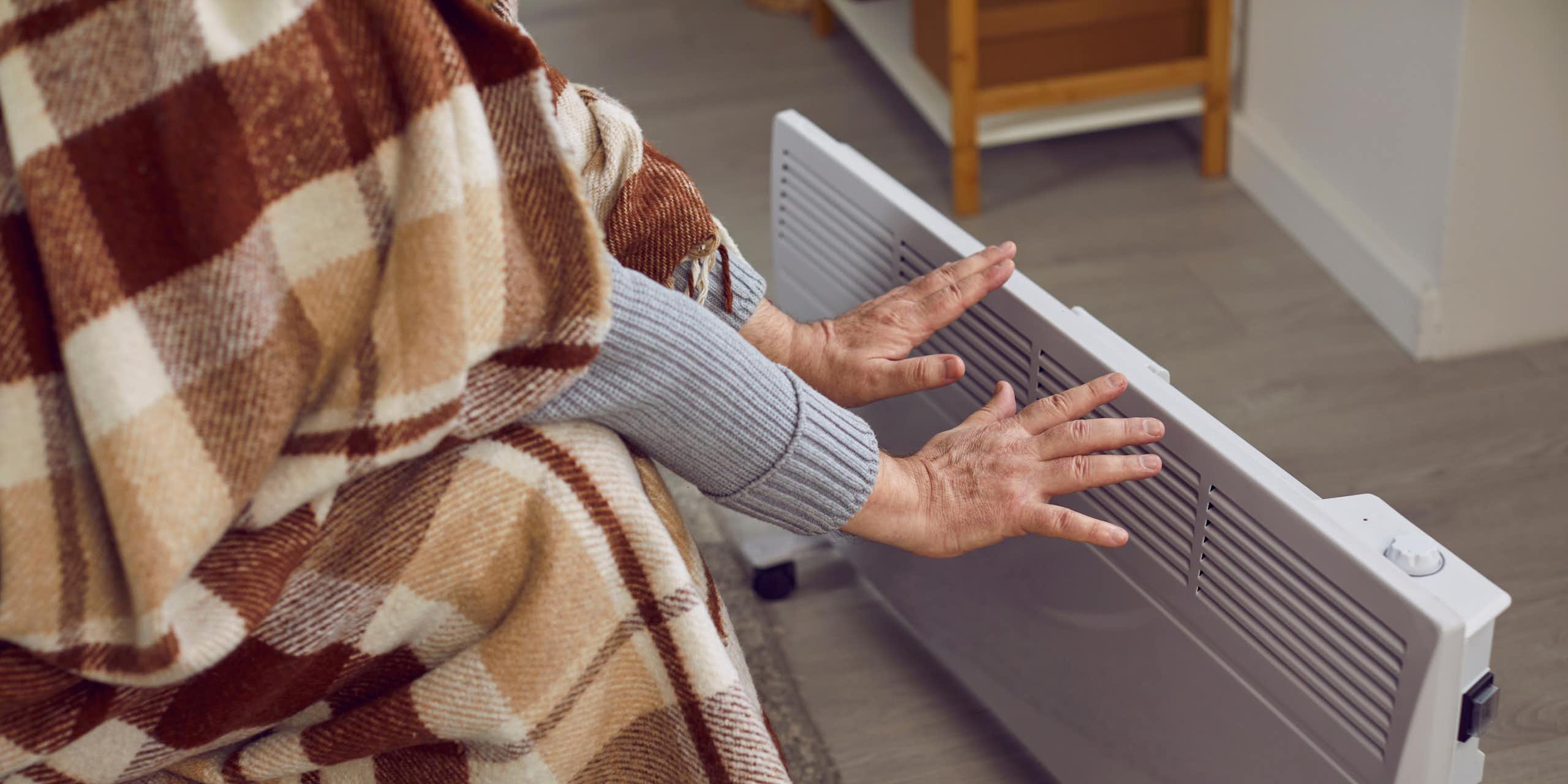 a person wrapped in a blanket holds their hands close to a portable heater