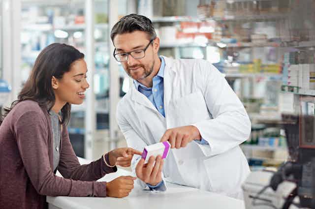 A male pharmacist shows a female customer a medicine packet.