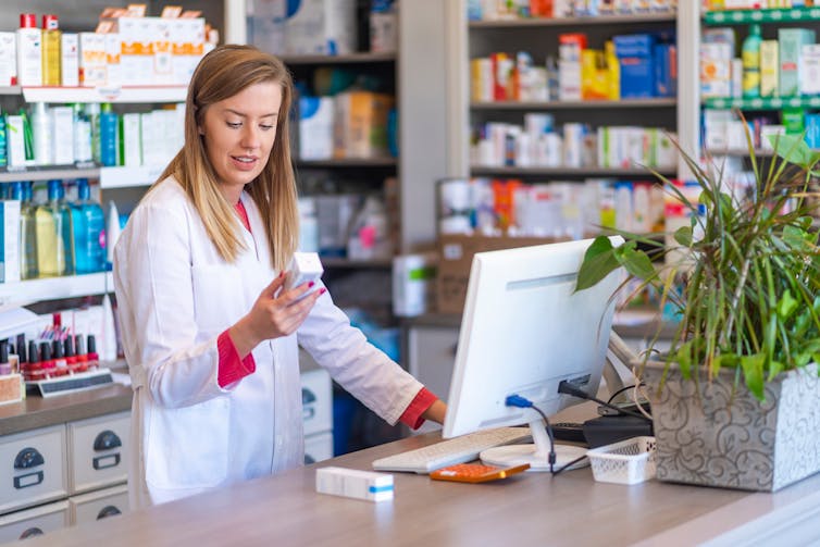 A female pharmacist is looking at a medicine box.