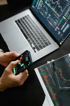 Person holding android smartphone near laptop showing stock price movements