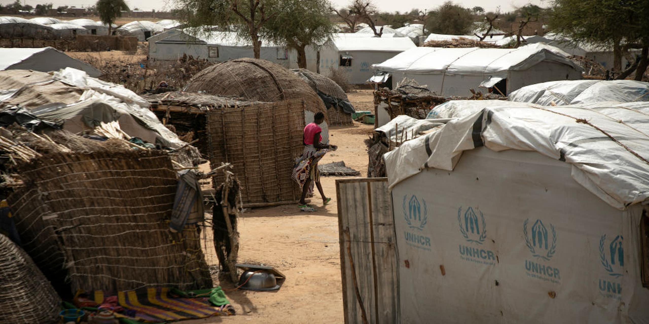 A woman walking between makeshift shelters and tents made with reeds and canvas.