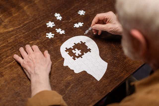 Elderly man doing a jigsaw puzzle in the shape of a human head