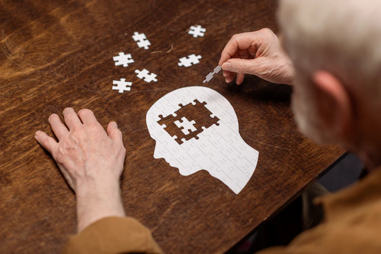 Elderly man doing a jigsaw puzzle in the shape of a human head