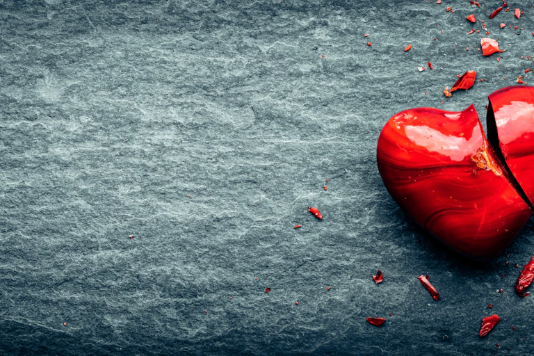 Image of a heart (perhaps ceramic), broken, against what looks like a hard stone background