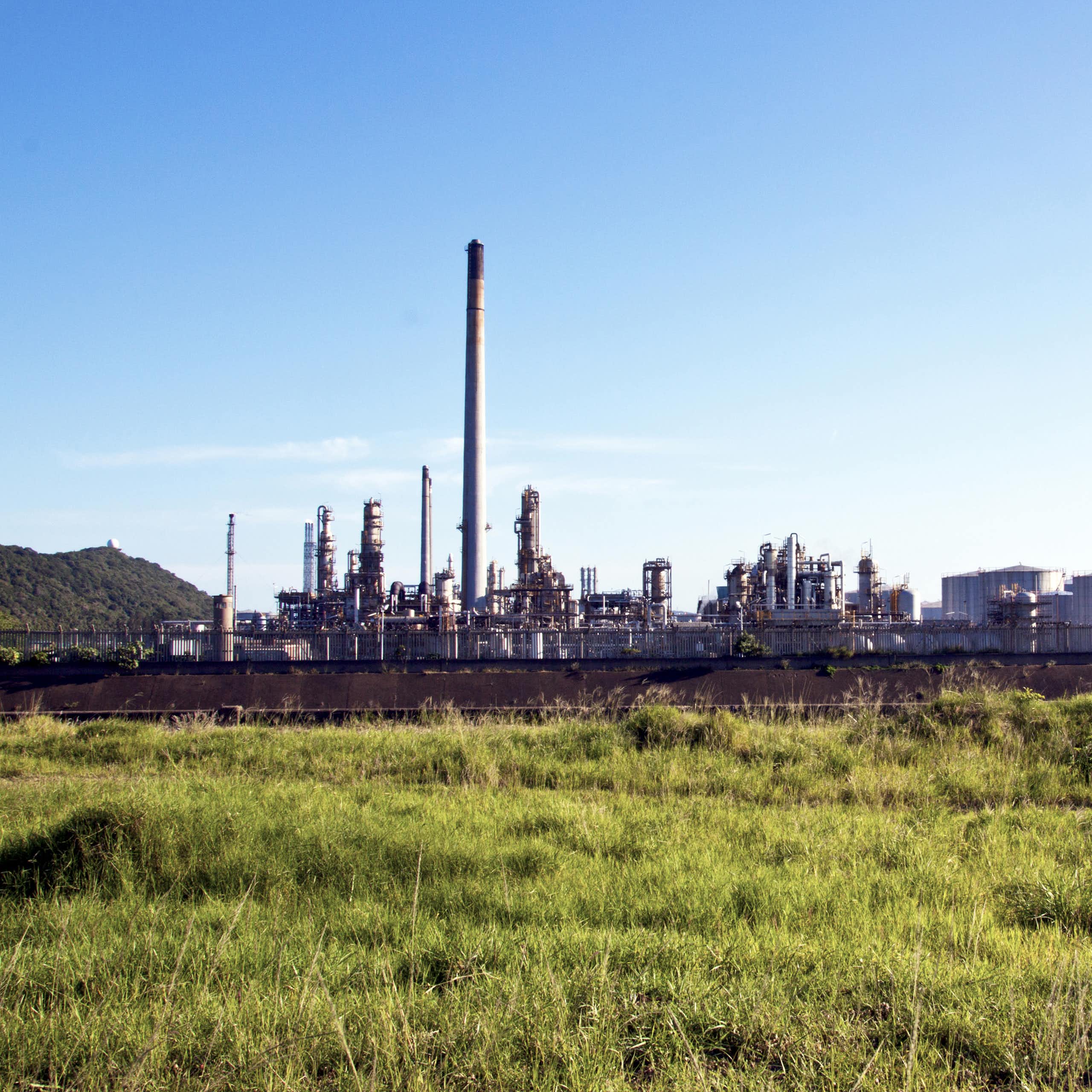 An oil refinery is seen with a grassy field in the back