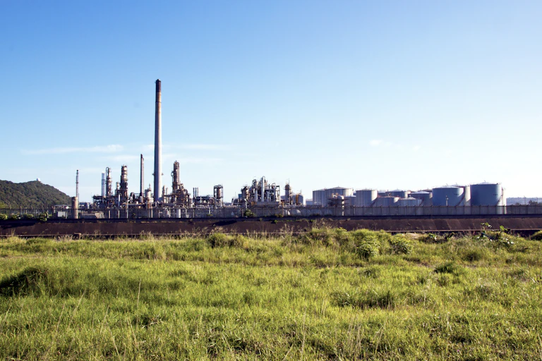 An oil refinery is seen with a grassy field in the back